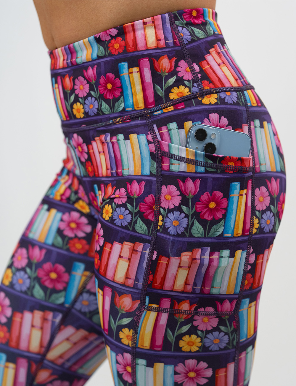 close up of the brightly colored books and flowers leggings pocket holding a phone against a white background