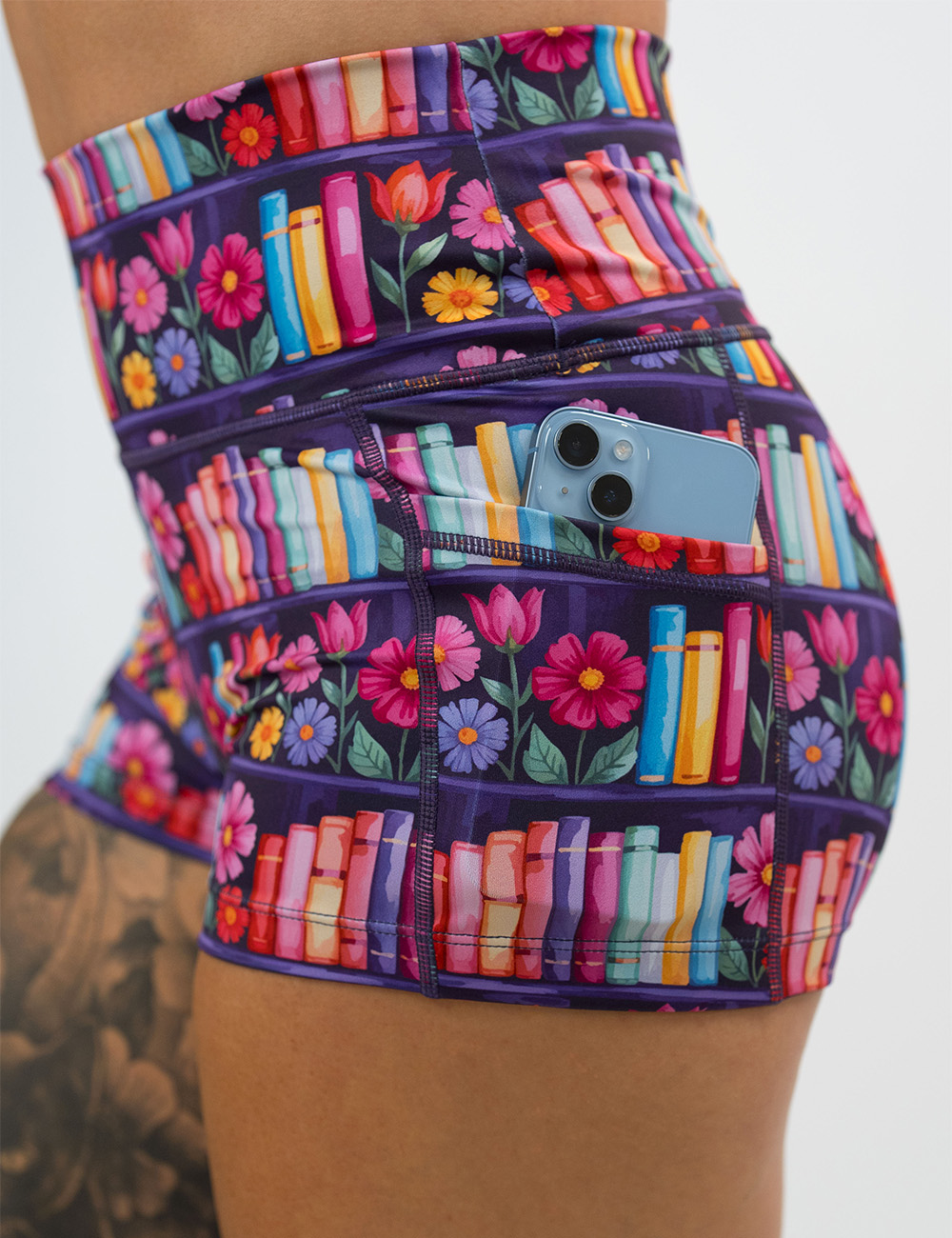 close up of the brightly colored books and flowers 2.5 inch shorts pocket holding a phone against a white background