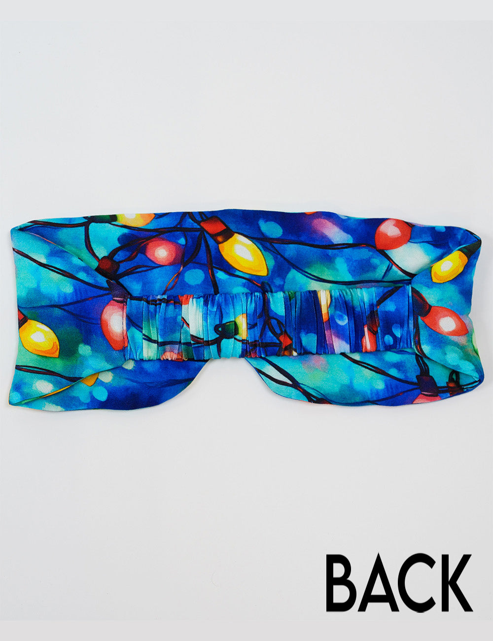 back of the Christmas lights in front of  blue and teal background eye mask against a white background