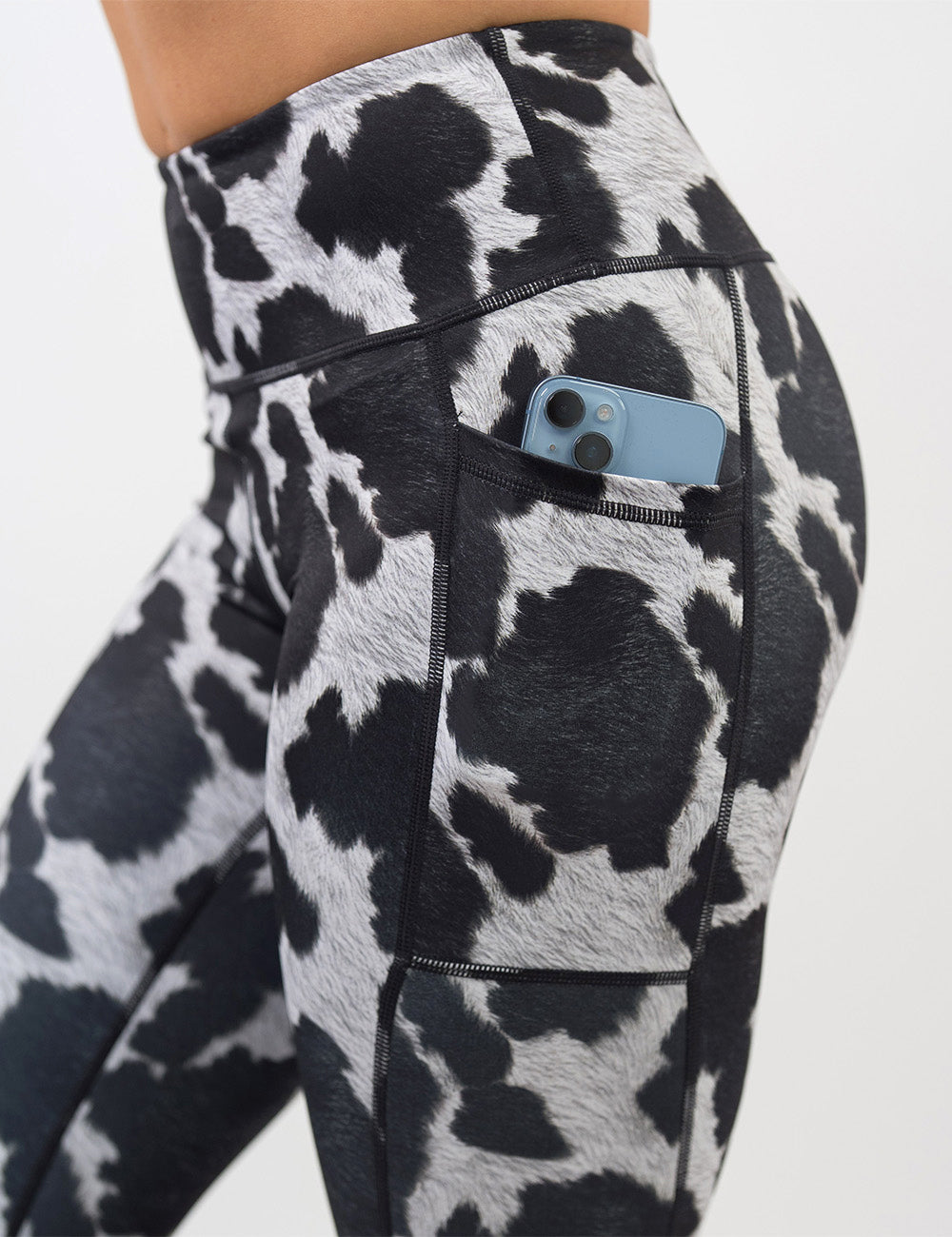 close up of the cow print leggings with a phone in its pocket against a white background