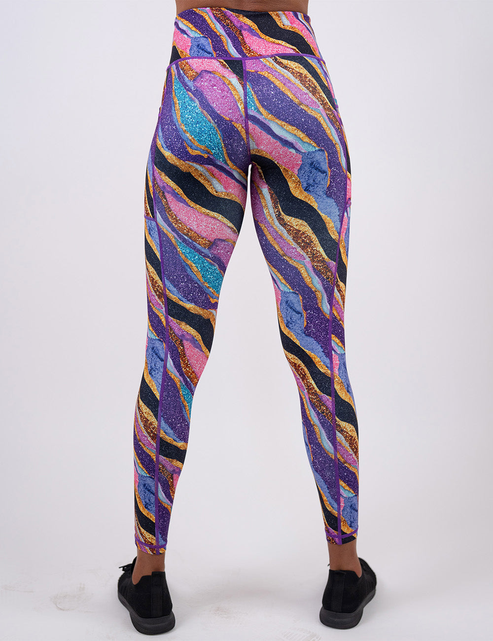 back of the purple, gold, black, blue, and pink abstract stripes full length leggings against a white background
