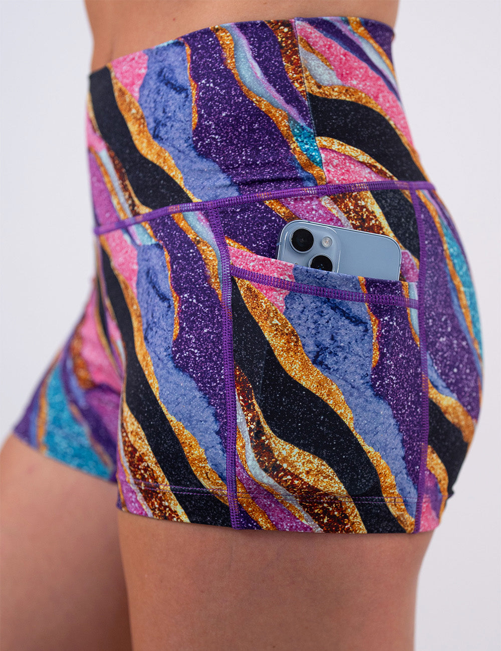 close up of the purple, gold, black, blue, and pink abstract stripes 2.5 inch shorts with a phone in its pocket
