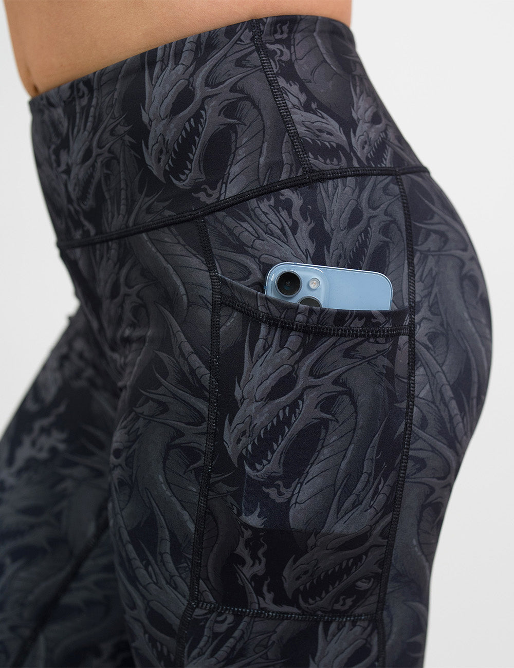 close up of the black leggings with grey dragons with a phone in its pocket