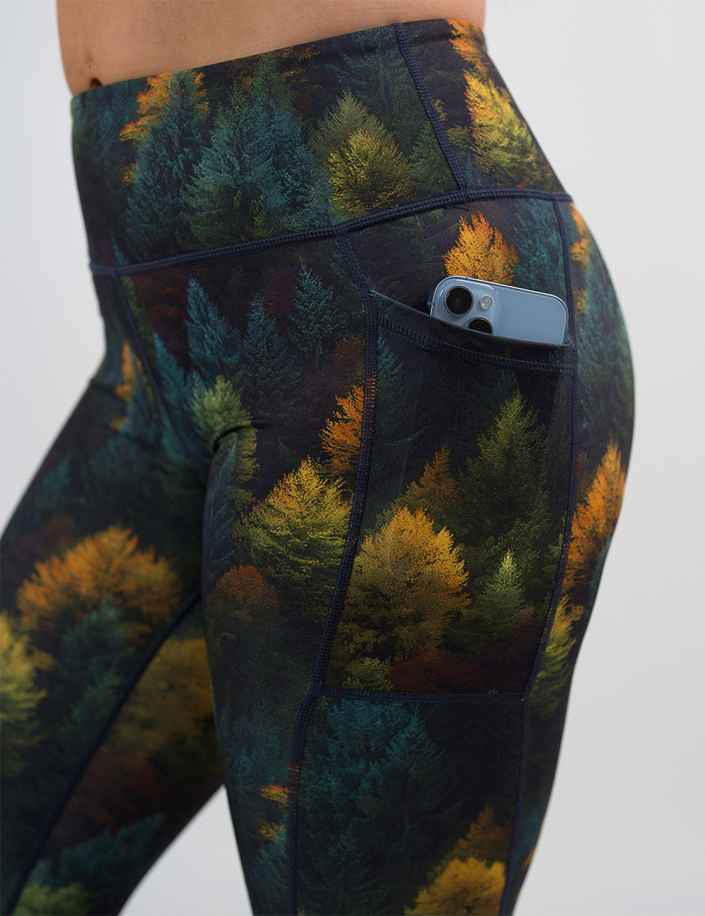 close up of the orange, green, and bluish green trees leggings with a phone in its pocket
