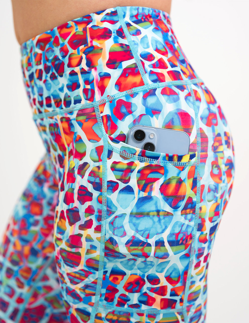 close up of the turquoise, coral, pink, orange, purple, and yellow mosaic style pattern leggings with a phone in its pocket