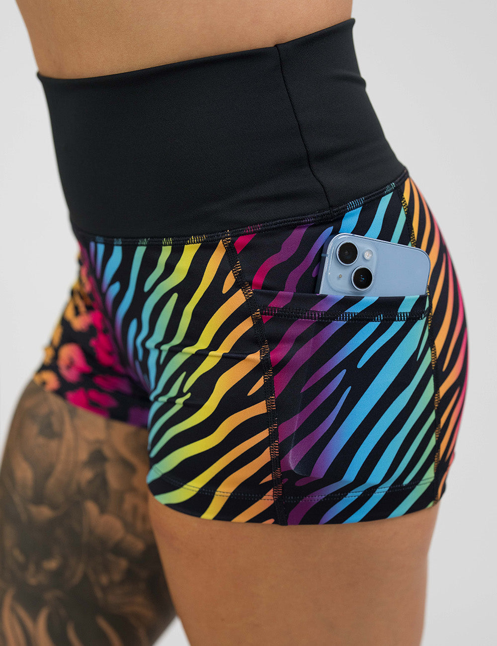 close up of the zebra and leopard rainbow print shorts showcasing the pocket with a phone it