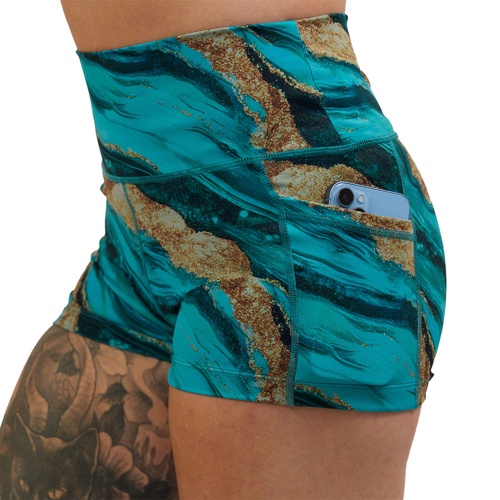 close up of the blue ocean with gold streaks patterned 2.5 inch shorts with a phone in the pocket against a white background