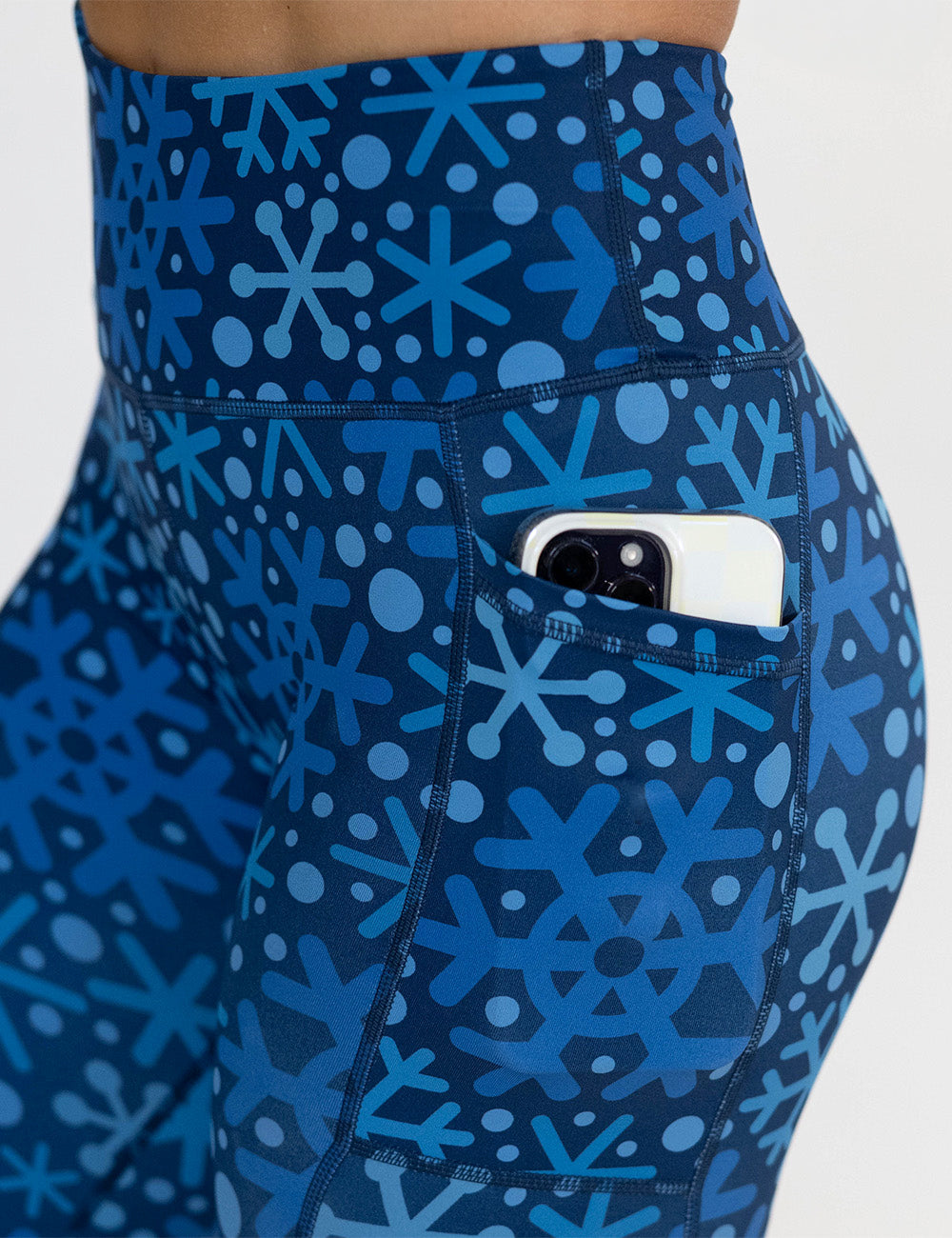 close up of the blue snowflakes on a dark blue background leggings with a phone in its pocket