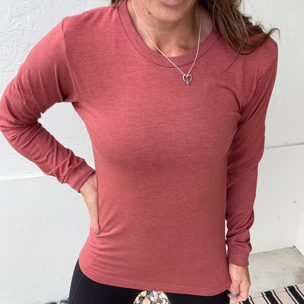 Person wearing a heather clay red long-sleeve shirt against a white wall