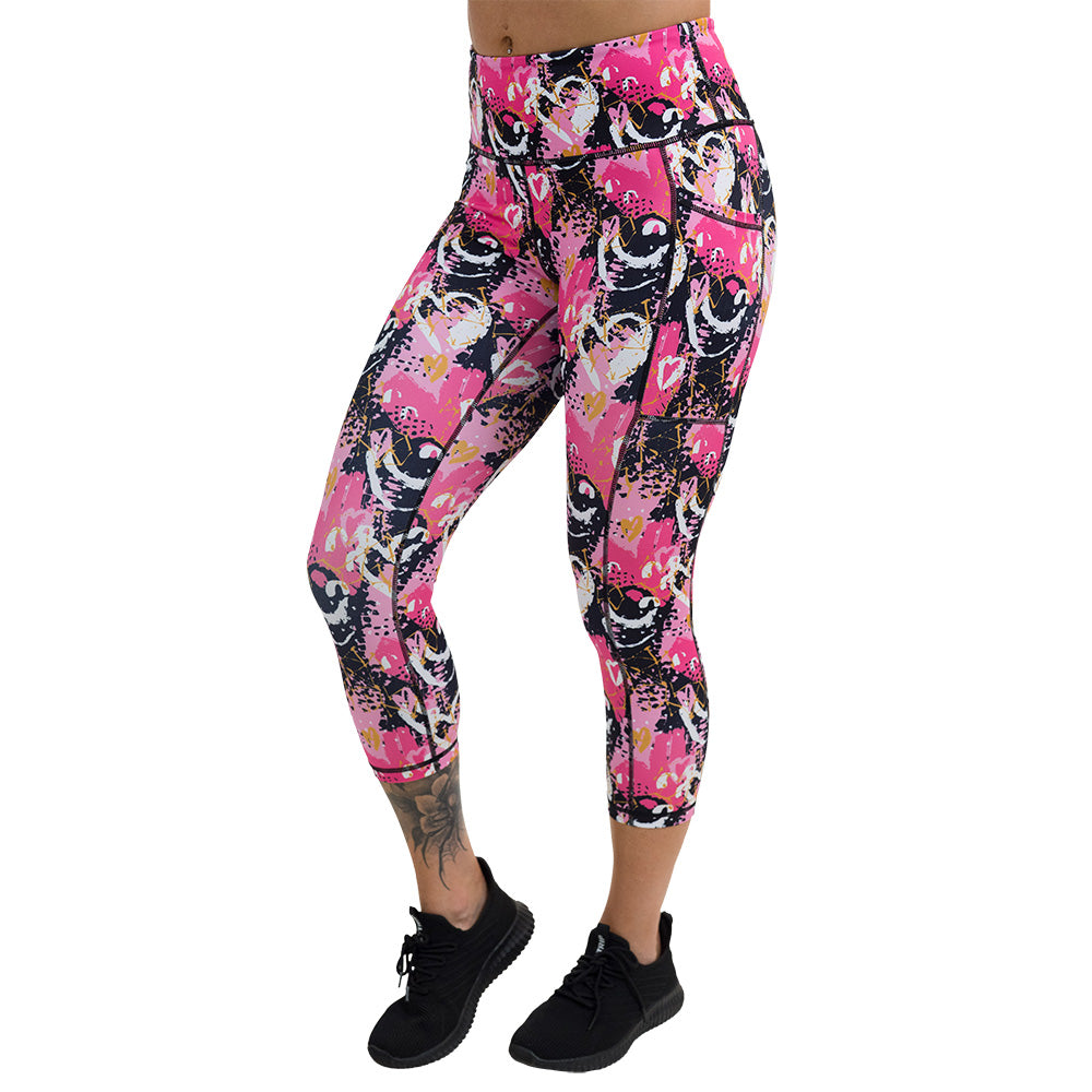 white hearts against a bold pink, black, and yellow pattern capri leggings against a white background