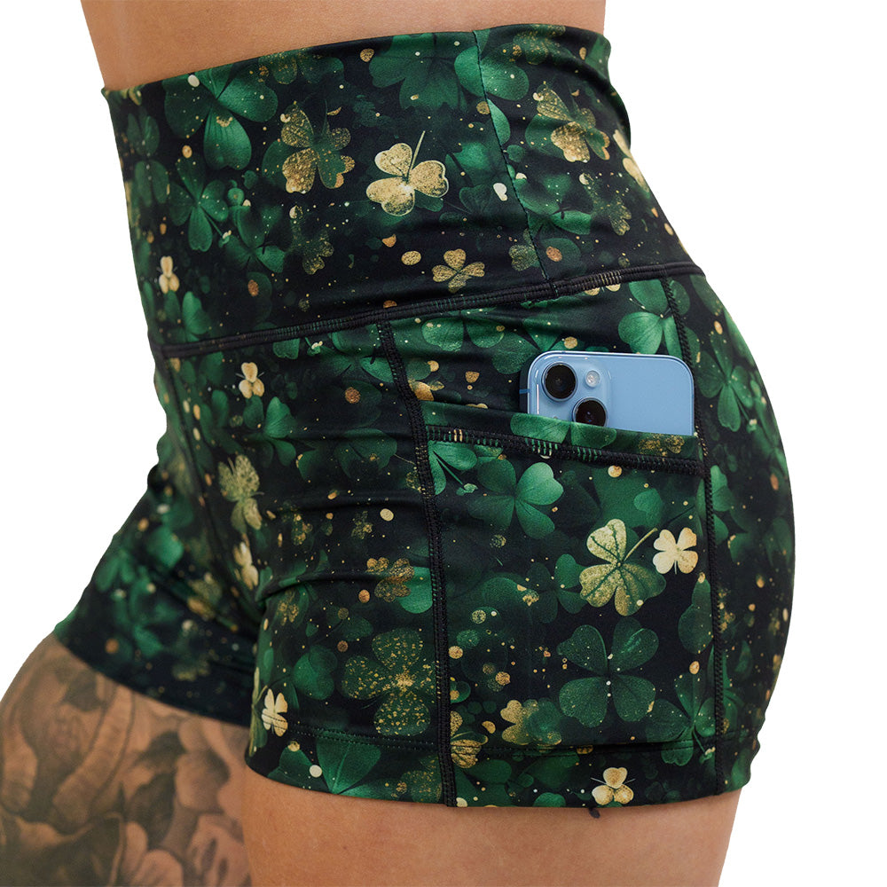 close up of the green and gold shamrock patterned 2.5 inch shorts with a phone in the pocket