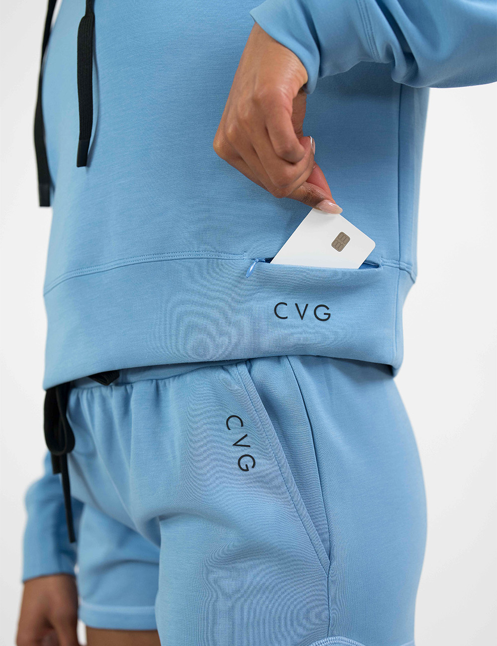 close up of the light blue sweatshirt with black drawstrings pocket holding a credit card against a white background