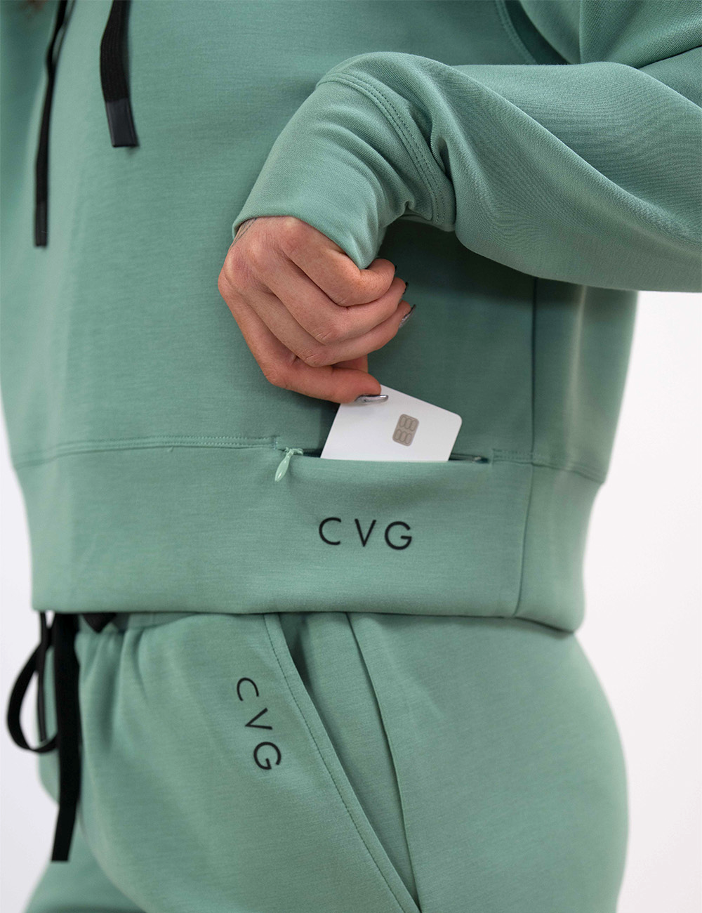 close up of the light green hoodie with black drawstrings pocket holding a credit card