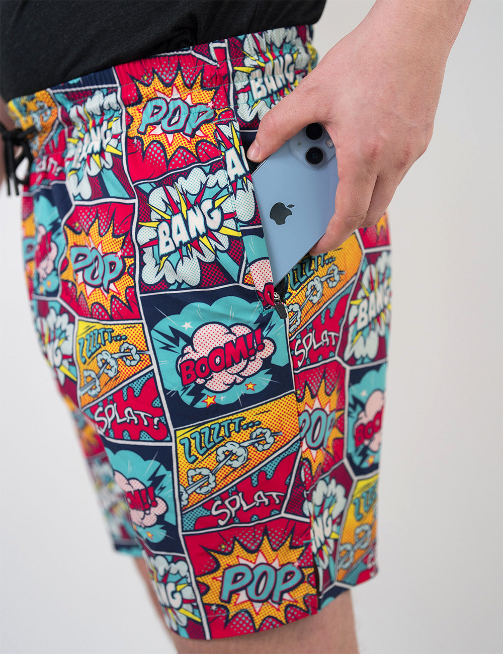 close up of the comic book panel themed men's shorts with a phone in its pocket against a white background