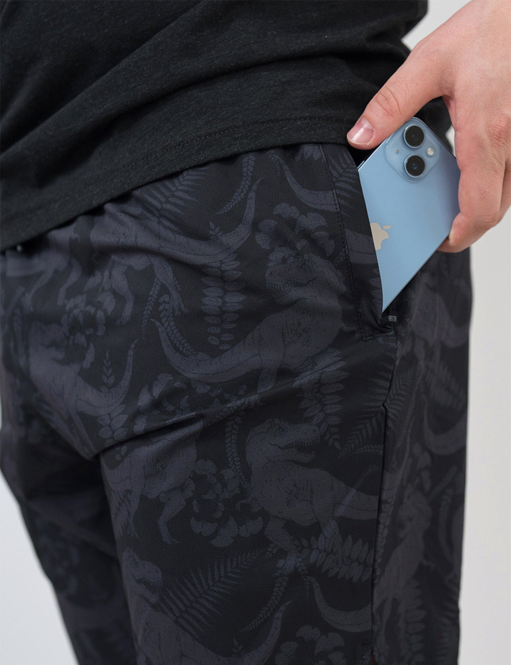 close up of the black men's shorts with a tonal grey t-rex pattern with a phone in it's pocket