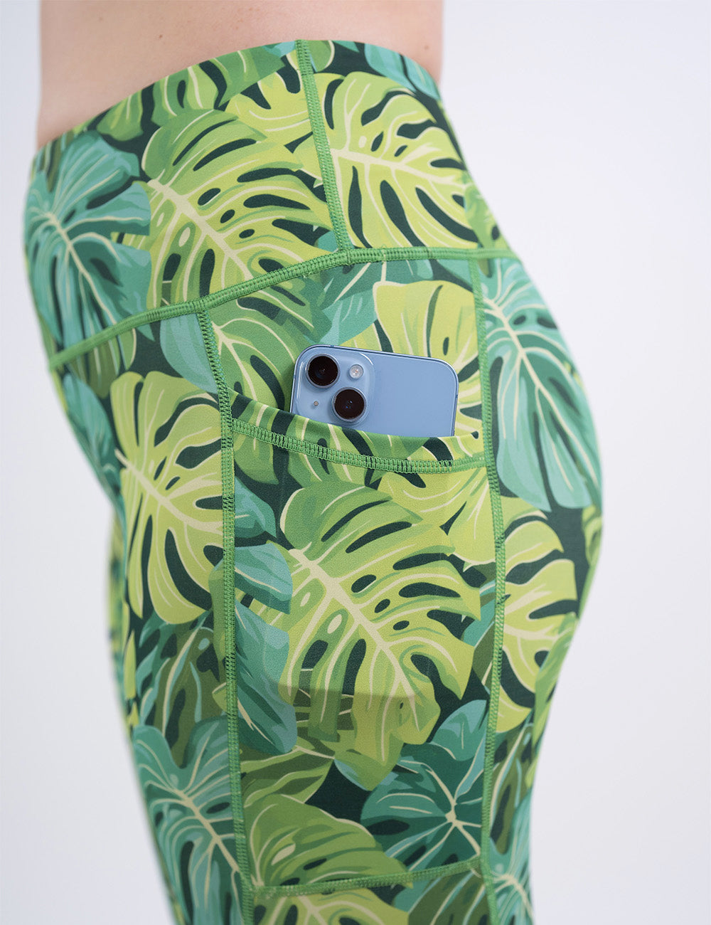 close up of a phone in the pocket of the green tropical leaves leggings against a white background