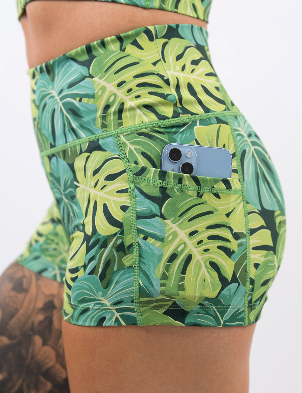 close up of a phone in the pocket of the 2.5 inch green tropical leaves shorts against a white background