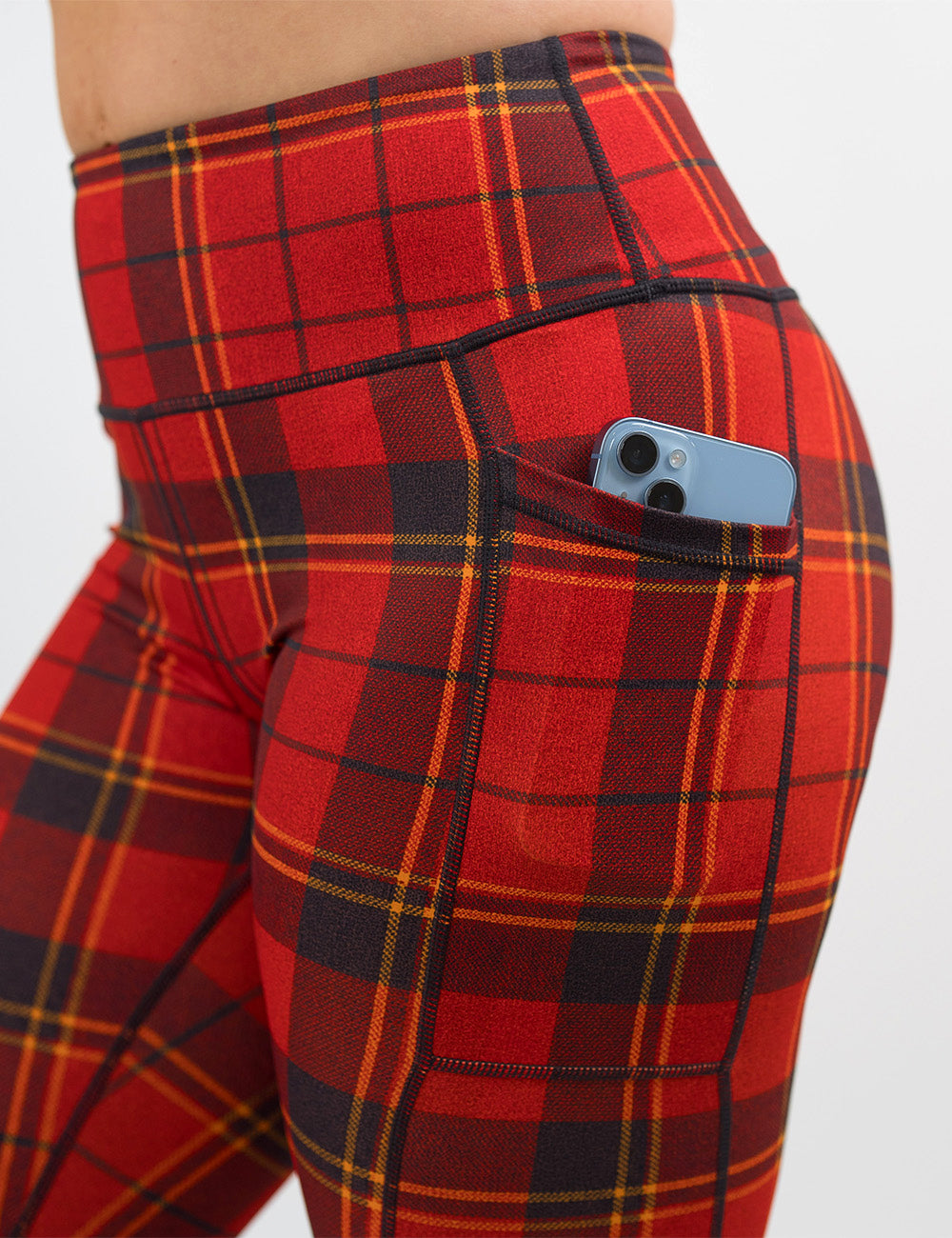 close up of the red, yellow, and dark grey plaid leggings with a phone in its pocket