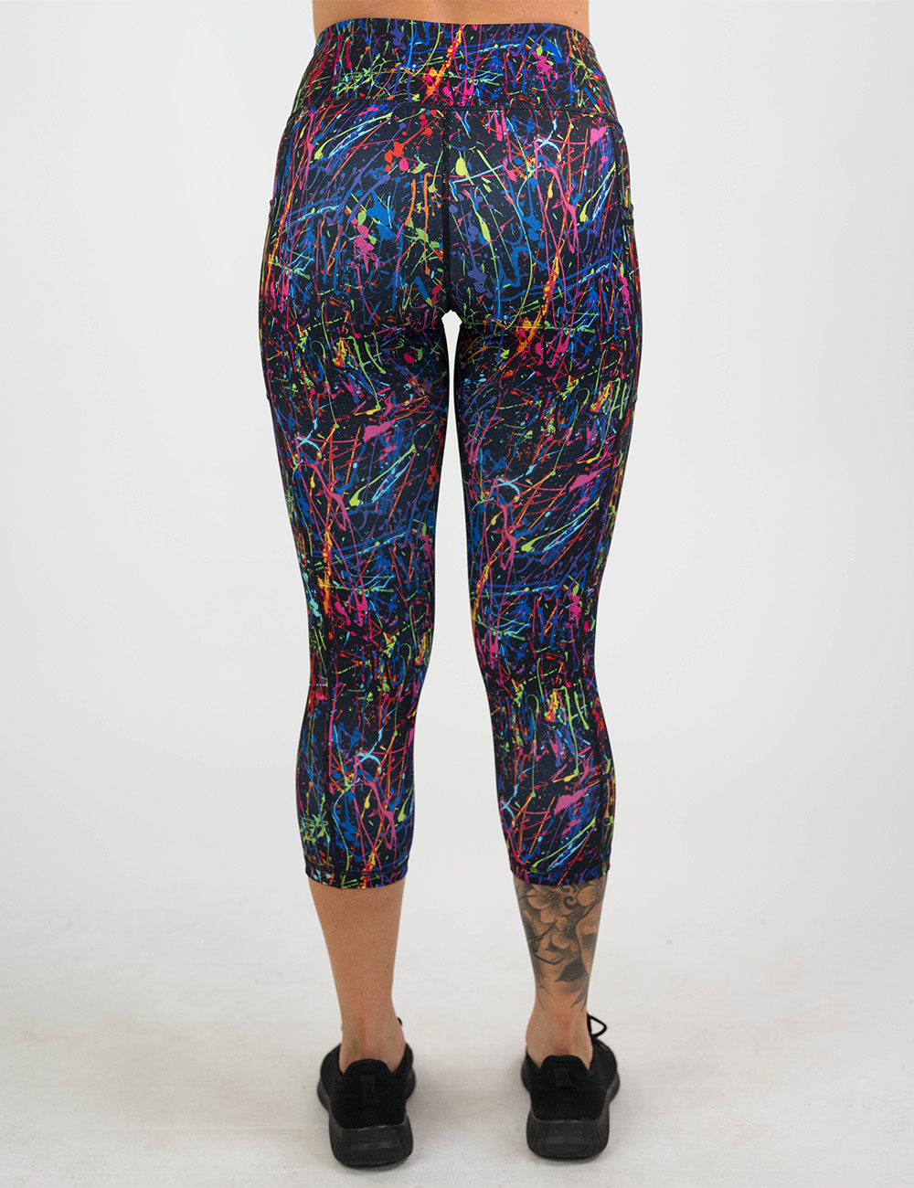 back of the rainbow paint splatter against a black background pattern capri leggings