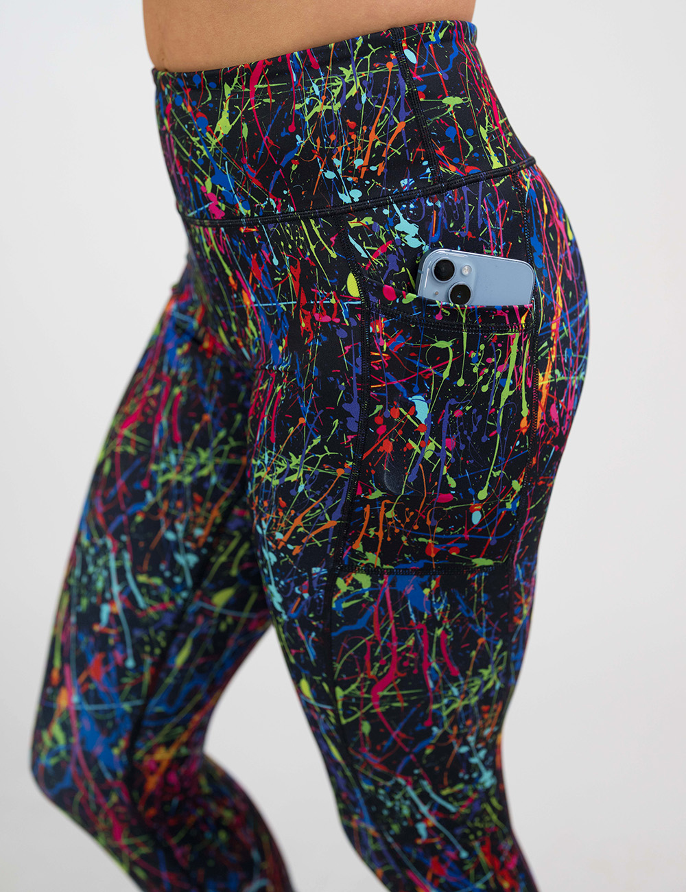 close up of the rainbow paint splatter against a black background pattern leggings with a phone in the pocket