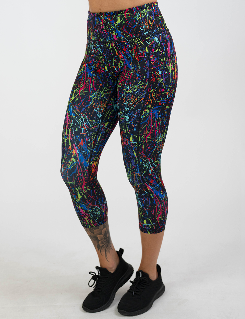 rainbow paint splatter against a black background pattern capri leggings facing the front against a white background
