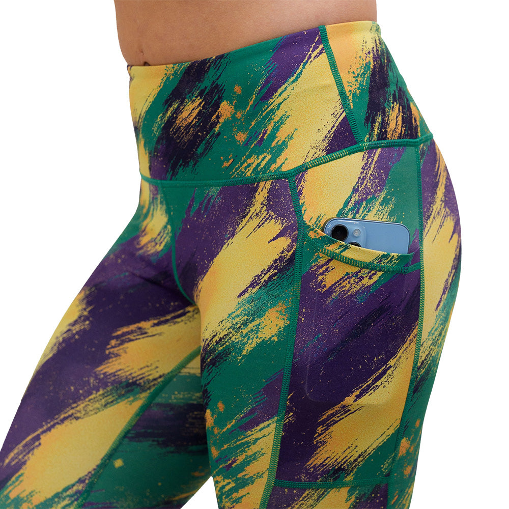 close up of the green, yellow. and purple patterned leggings with a phone in the pocket against a white background