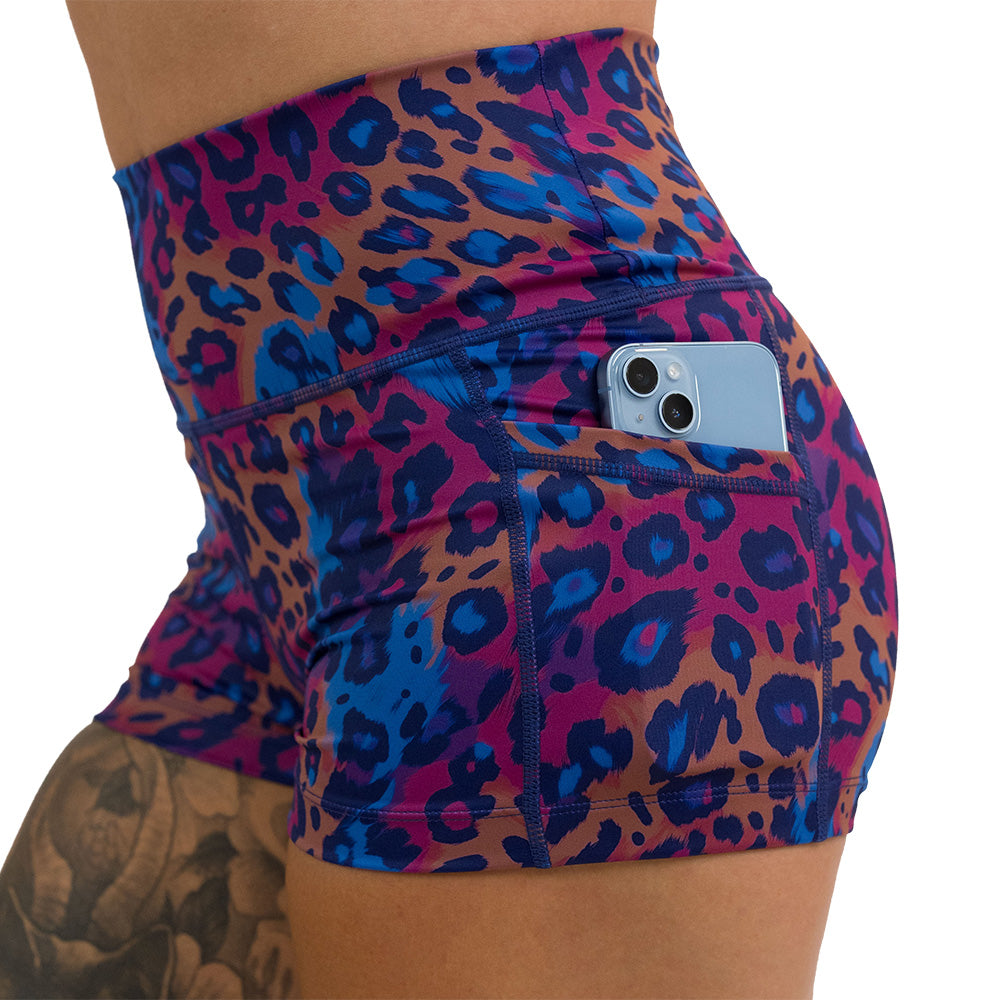 close up of a phone in the pocket of the 2.5 inch cheetah print against a yellow, blue, and purple background pattern shorts