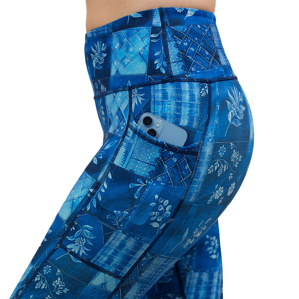 close up of the blue patch work pattern with plant designs leggings against a white background with a phone in its pocket