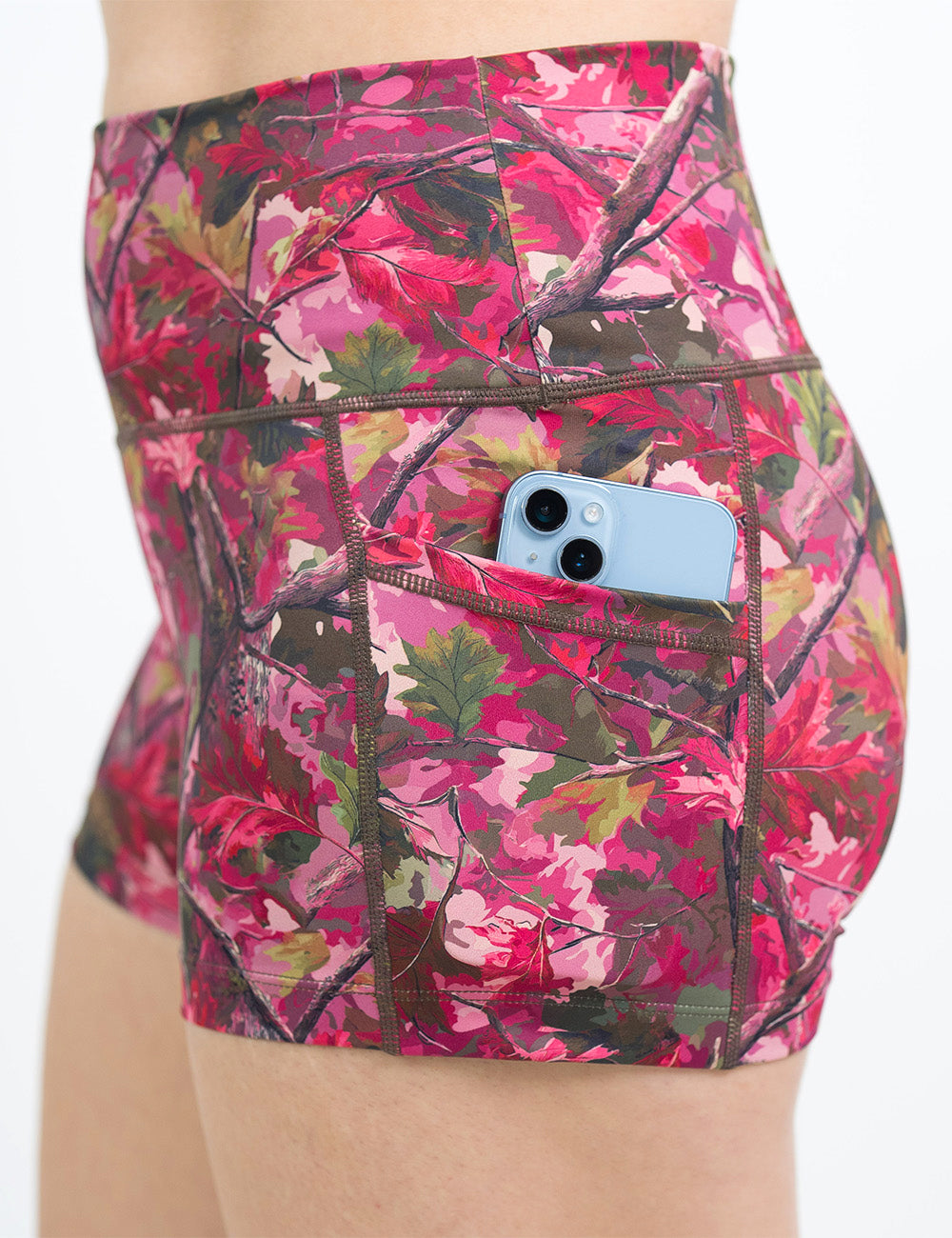 side view of the 2.5 inch pink forest camo shorts with a phone in its pocket