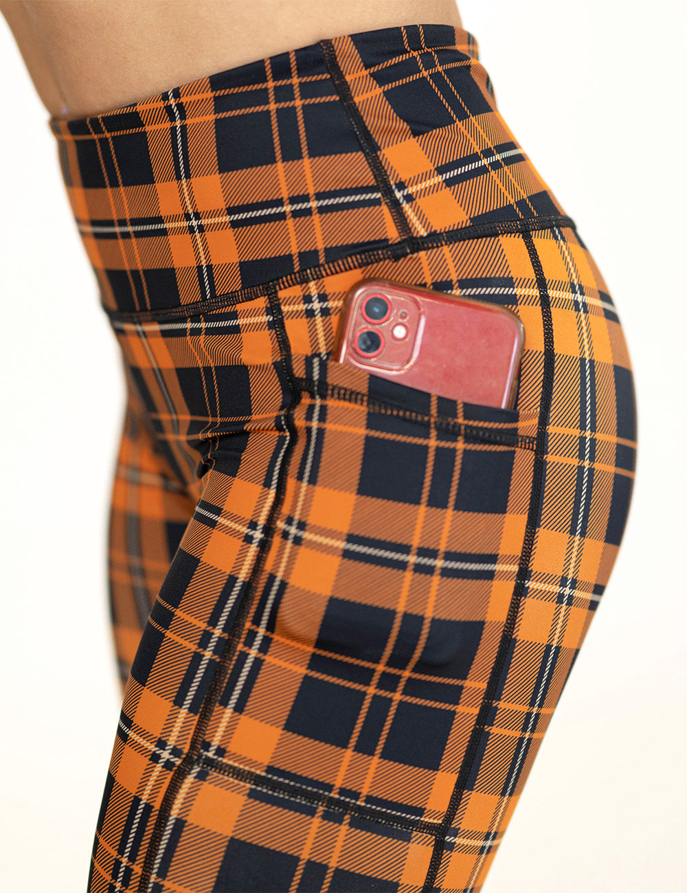 close up of the black and orange plaid leggings with a phone in its pocket
