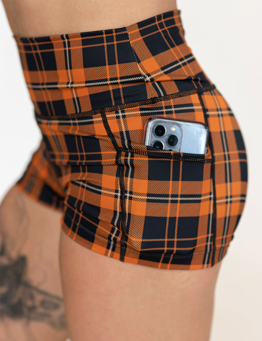 close up of the 2.5 inch black and orange plaid shorts with a phone in its pocket