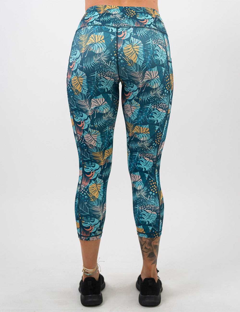 back of the capri blue, pink, yellow, and red tropical leaves leggings against a white background