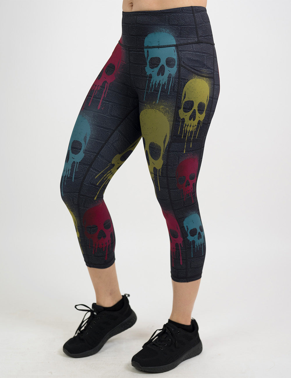front of the black brick capri leggings with spray painted red, yellow, and blue skulls all over against a white background