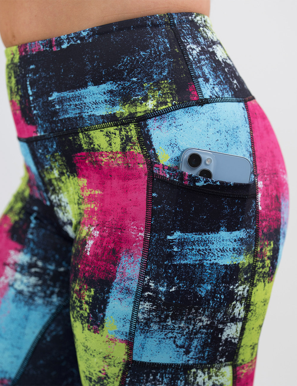 close up of the green, pink, and blue grunge pattern leggings with a phone in its pocket