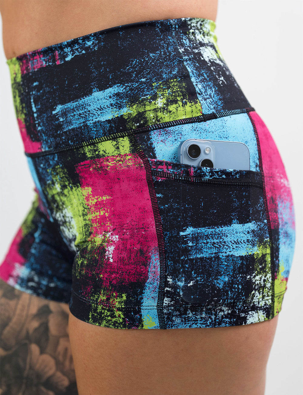 close up of the green, pink, and blue grunge pattern 2.5 inch shorts with a phone in its pocket