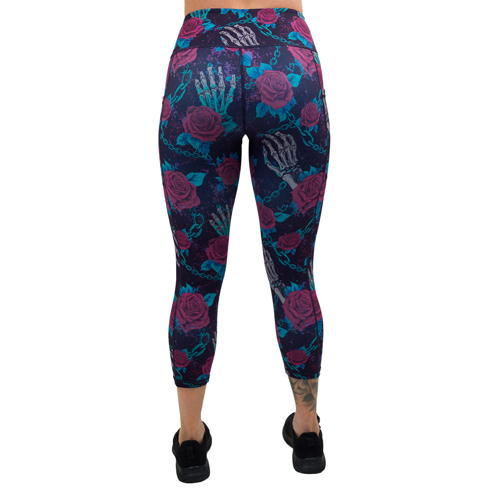 back of the roses and skeleton hands connected by chain links pattern capri leggings against a white background