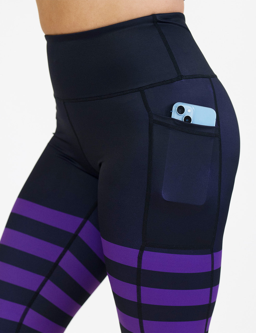 close up of the black with purple horizontal stripes leggings with a phone in its pocket