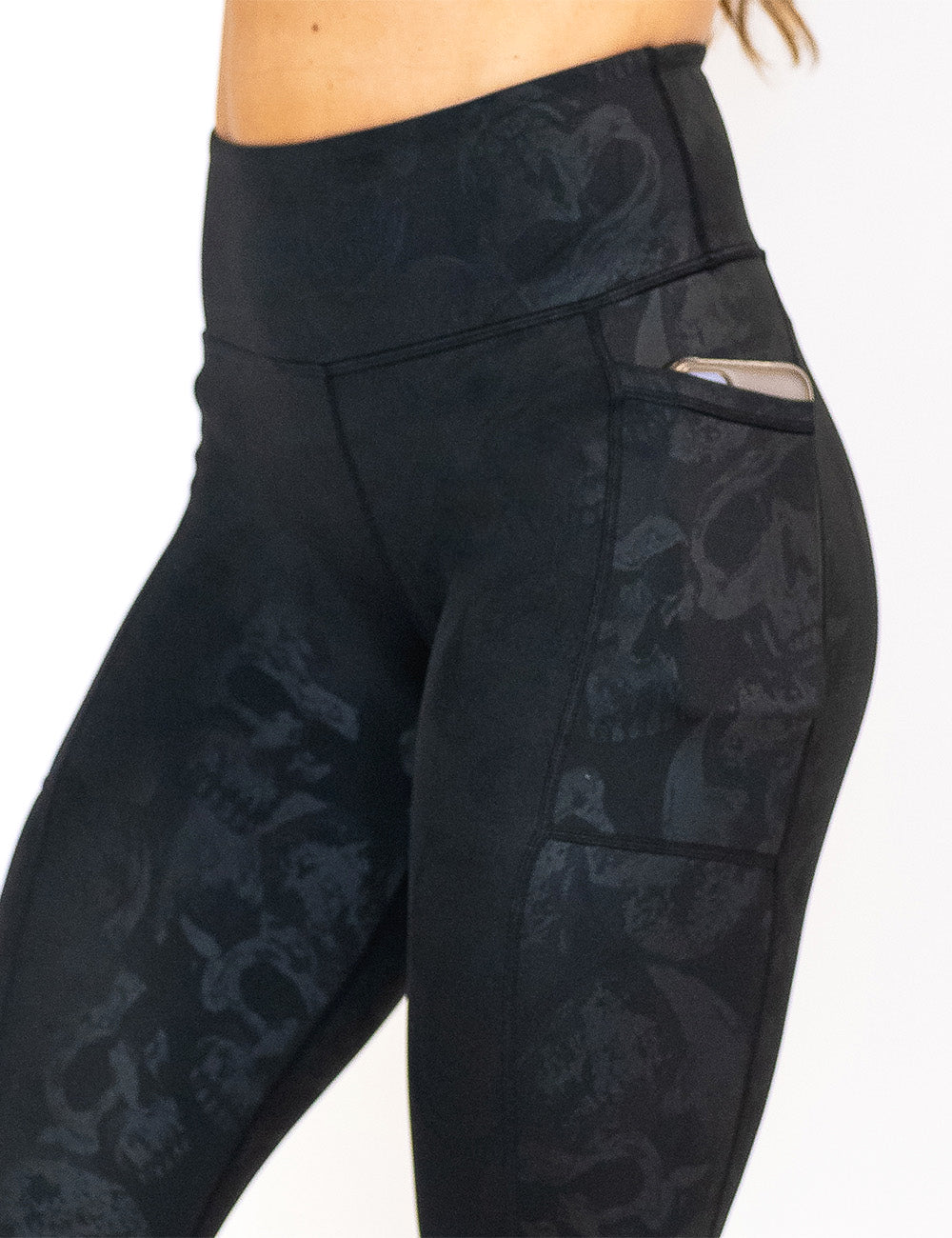 close up of the black leggings with a dark grey skull pattern with a phone in its pocket