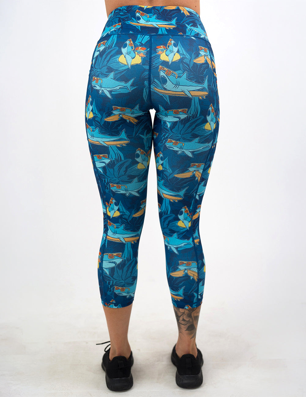back of the cartoon sharks surfboarding with sunglasses capri leggings against a white background