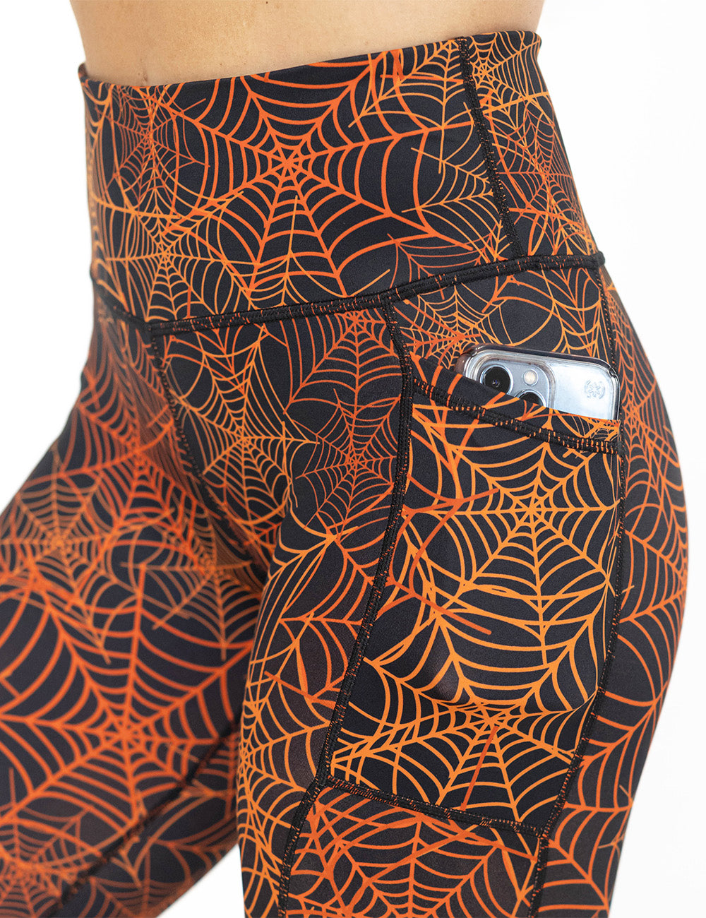 close up of the orange spider webs against a black background leggings with a phone in its pocket