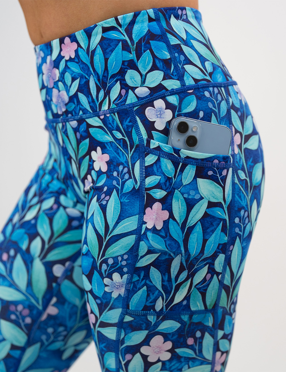 close up of the blue flowers and vines leggings pocket with a phone inside against  a white background