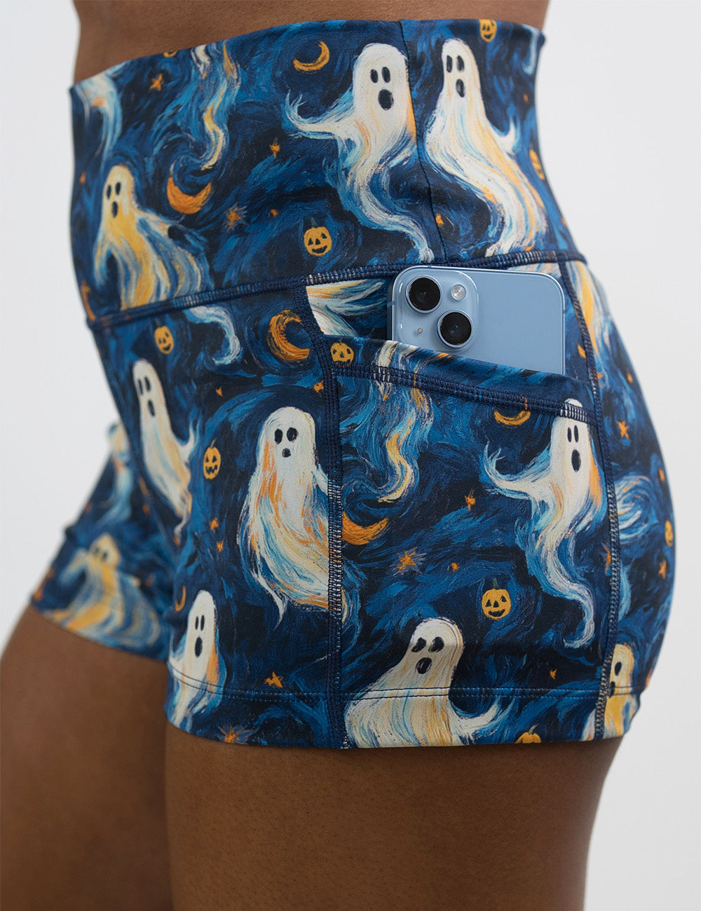 close up of the starry night ghosts against a blue background pattern 2.5 inch shorts with a phone in its pocket
