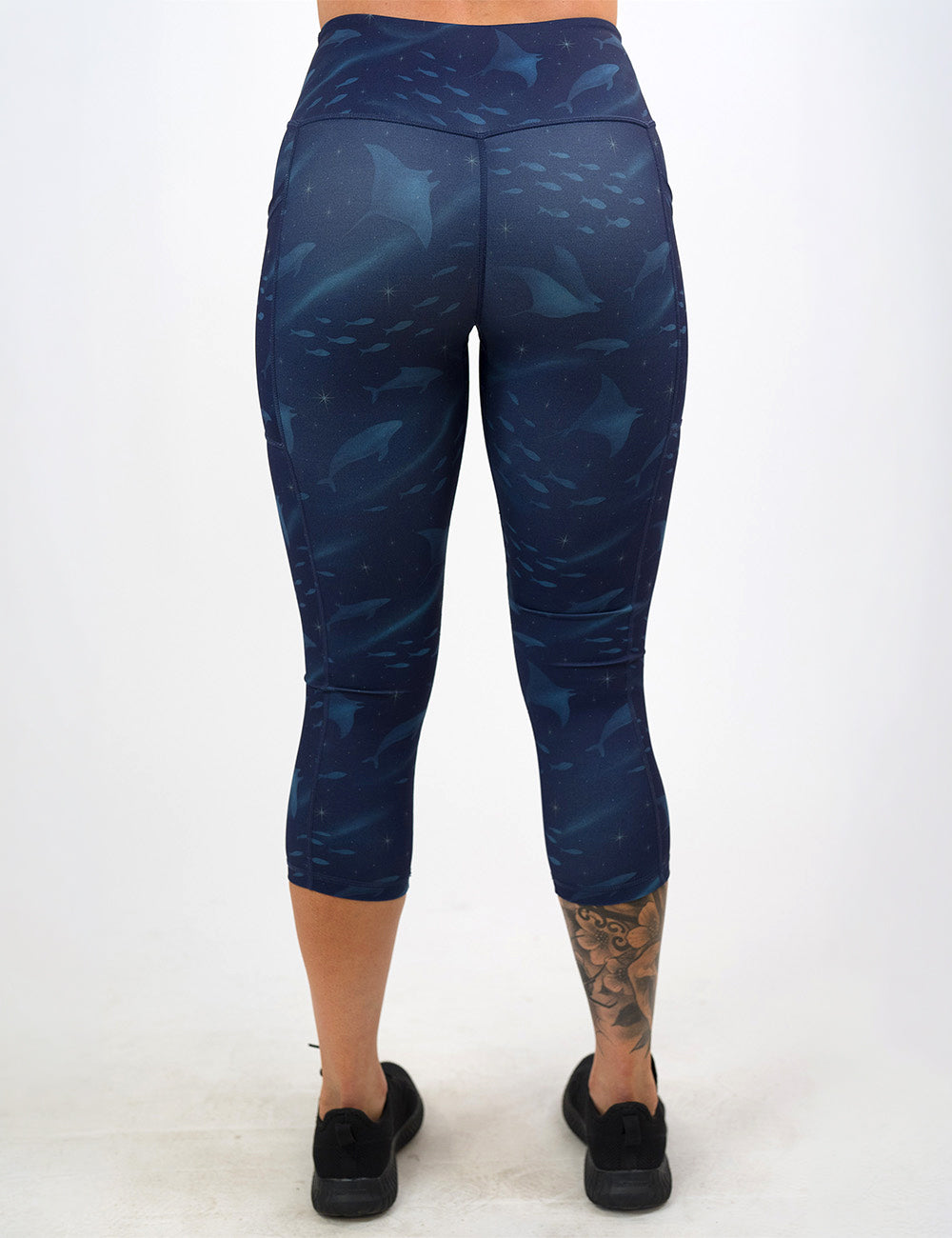 back of the dark blue ocean filled with sting rays, whales, and fish capri leggings against a white background