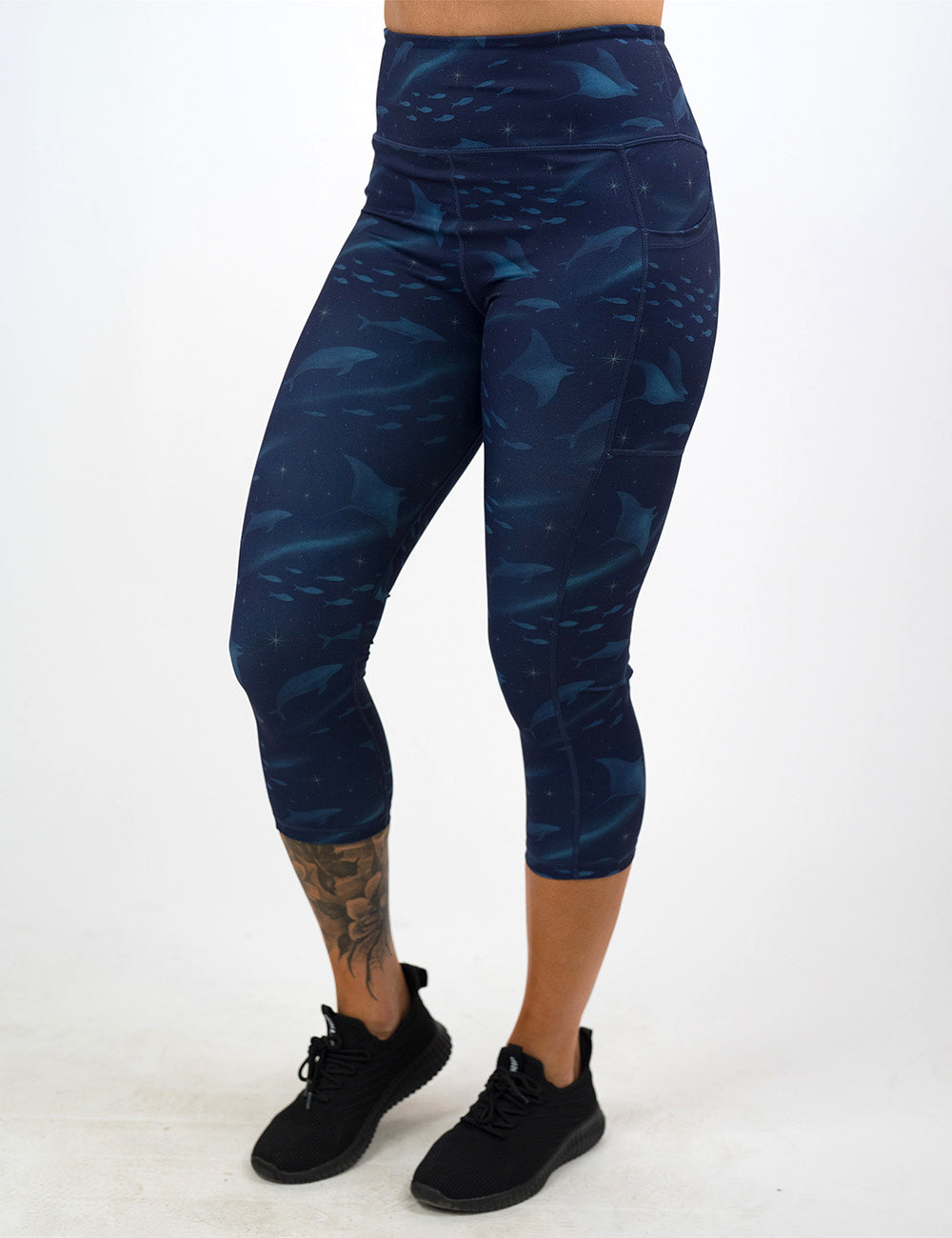 front of the dark blue ocean filled with sting rays, whales, and fish capri leggings against a white background