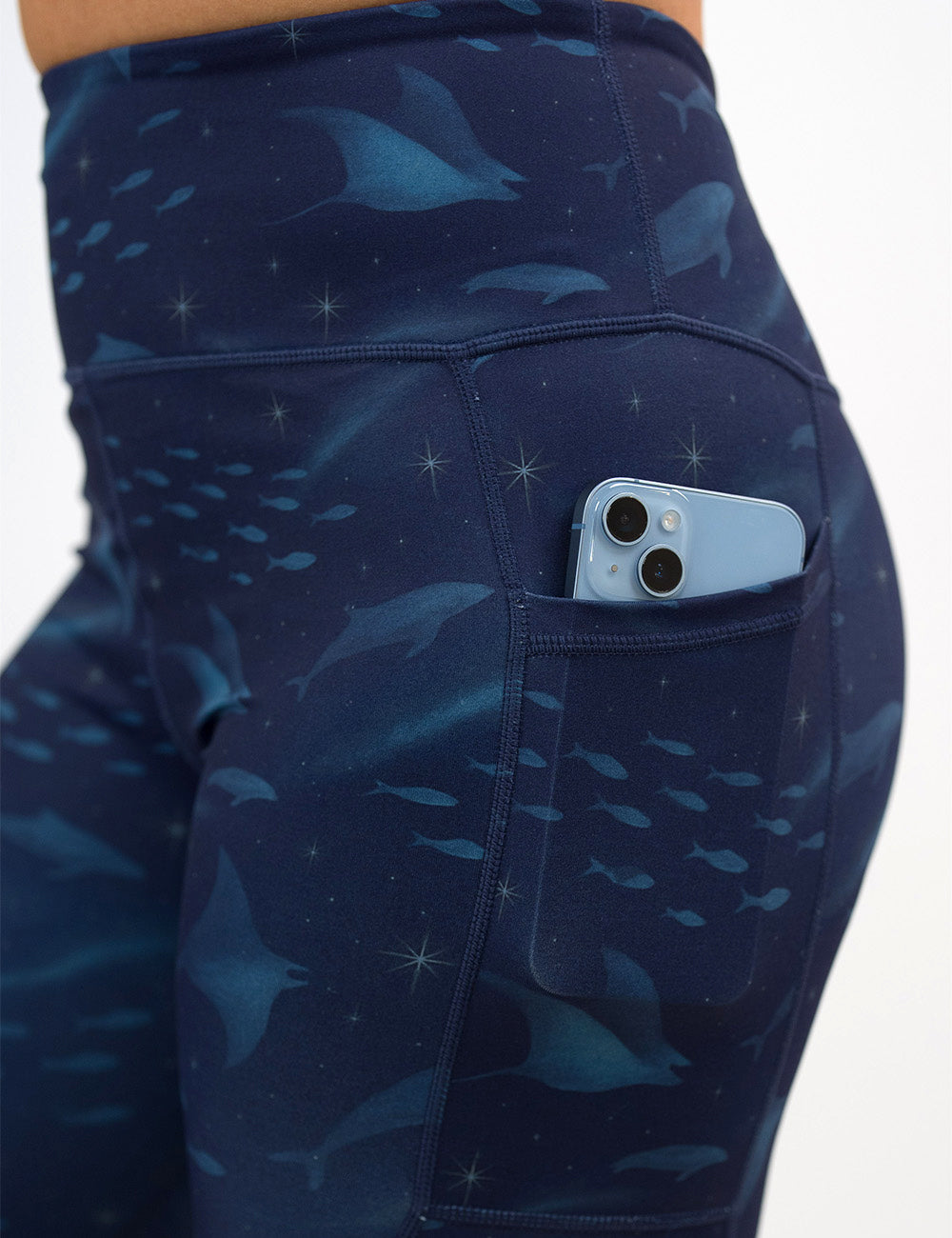 close up of the dark blue ocean filled with sting rays, whales, and fish leggings with a phone in the pocket