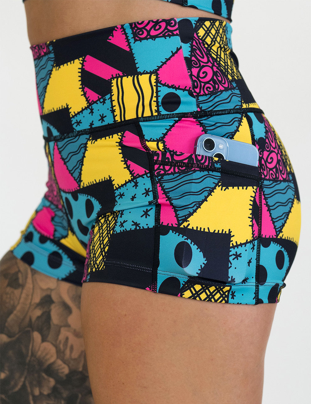 close up of the 2.5 inch yellow, teal, and pink patchwork design shorts with a phone in its pocket