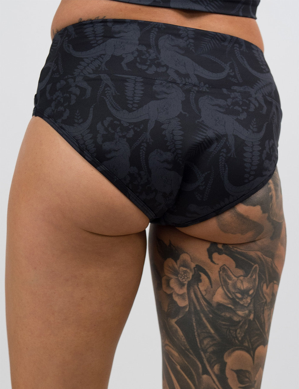 back of the black bathing suit bottoms with a grey dinosaur pattern against a white background
