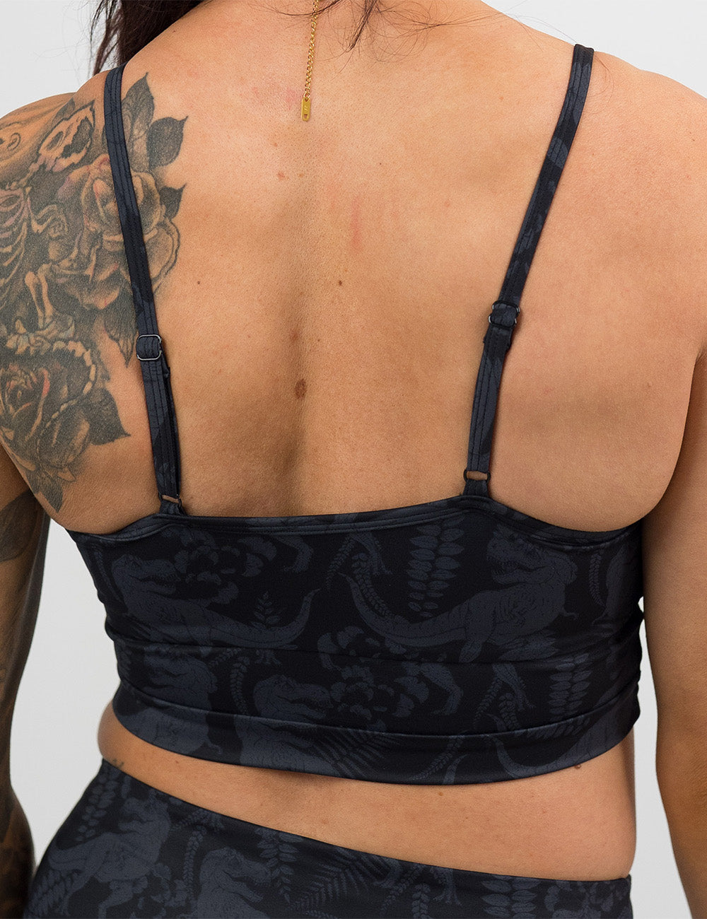 back of the black swimsuit with a grey dinosaur pattern against a white background