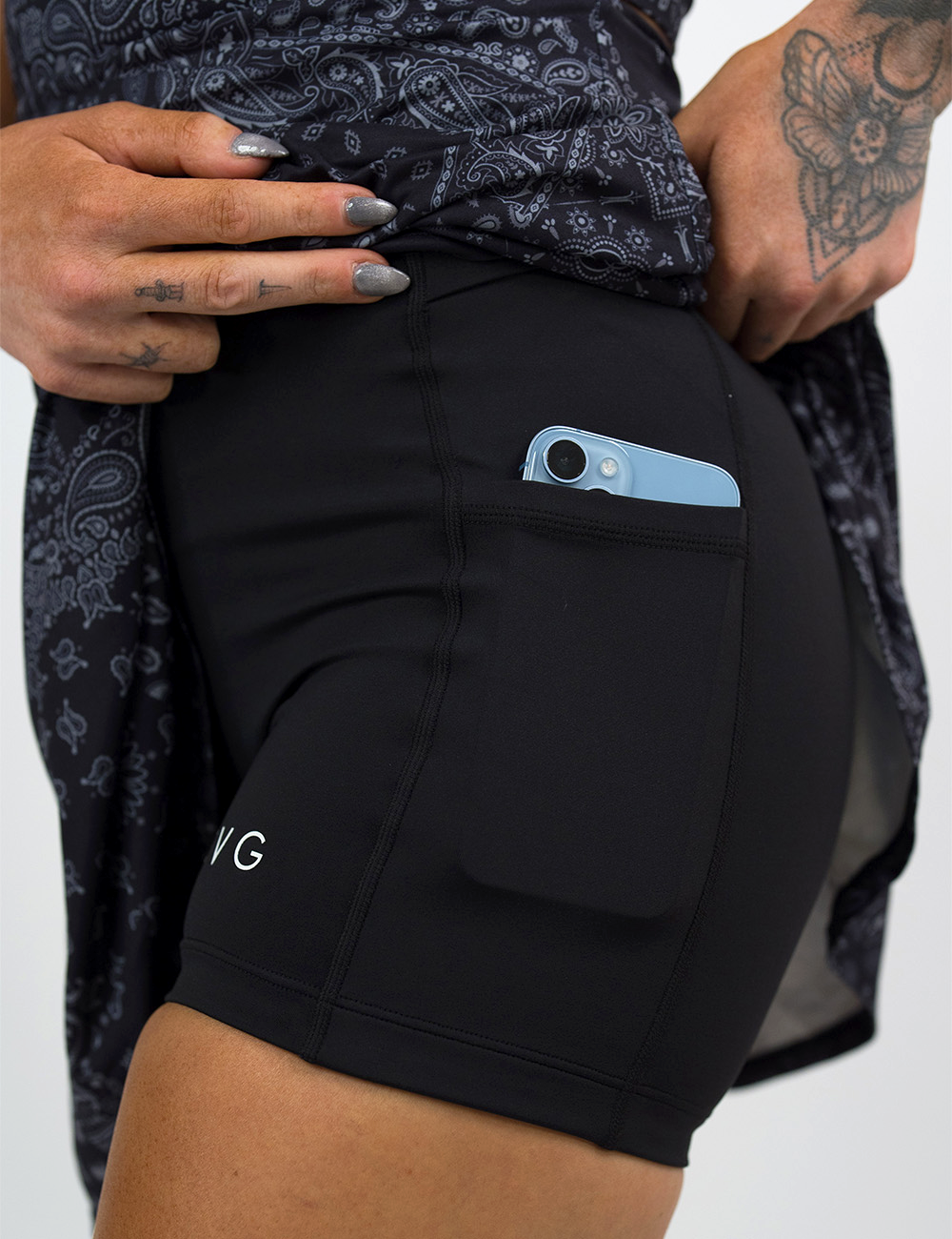 the black active dress with white accents rolled up to show the built in shorts holding a phone