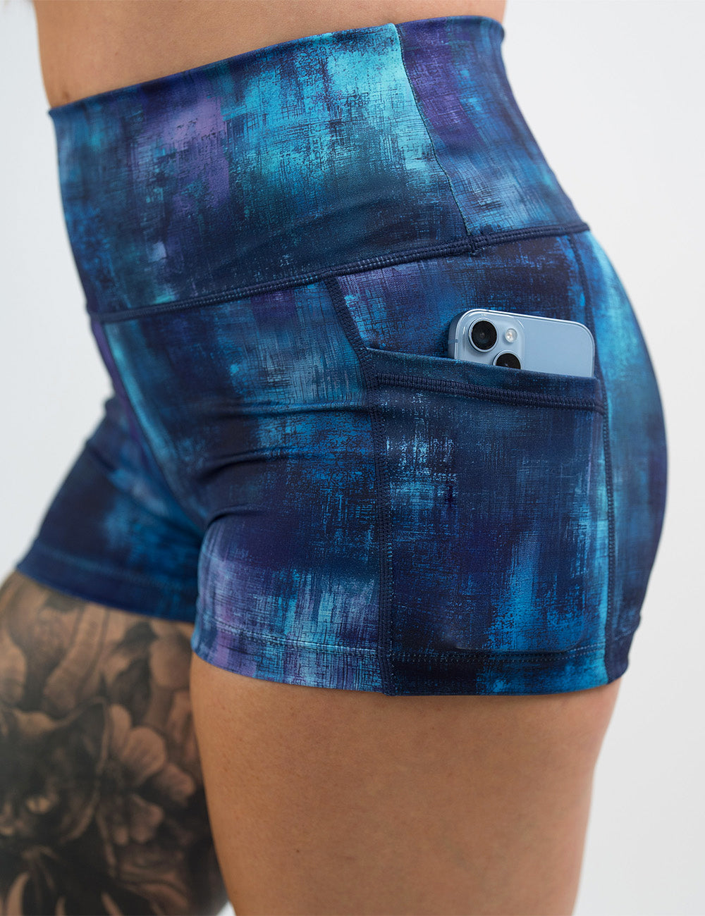 close up of the blue, teal, and purple grunge concrete pattern 2.5 inch shorts with a phone in its pocket